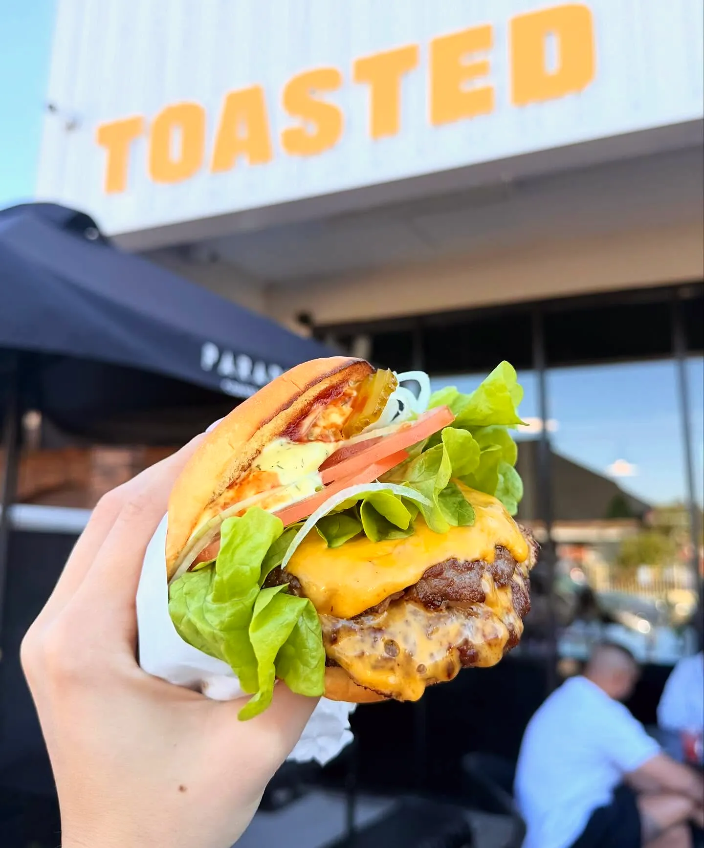 A smash burger held up in front of the TOASTED sign