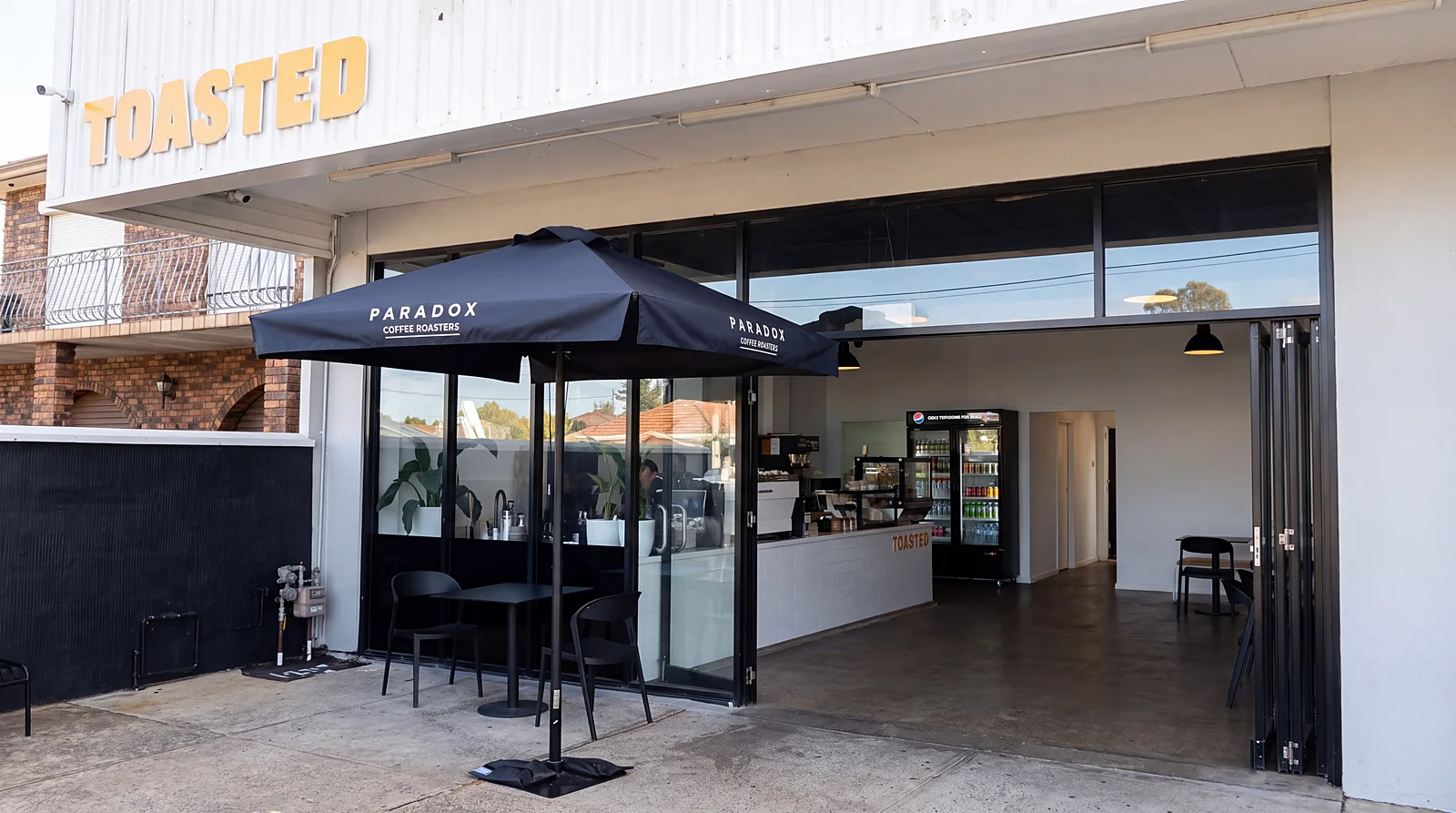 The TOASTED shopfront on Rawson Rd with its black Paradox Coffee umbrella and tables out front
